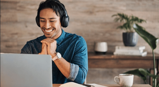 A man is sitting smiling at a laptop during a video call