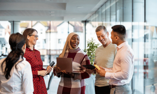 Group of colleagues chatting and smiling in a modern office hallway.